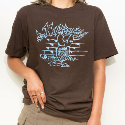 Alternate image - female model wearing artist Stimpies’ brown t-shirt with a cyan blue print on top depicting a cracked Humpty Dumpty.